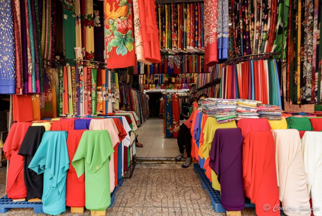 colorful fabrics hanging from ceiling and on mannequins in fabric market stall in Vietnam
